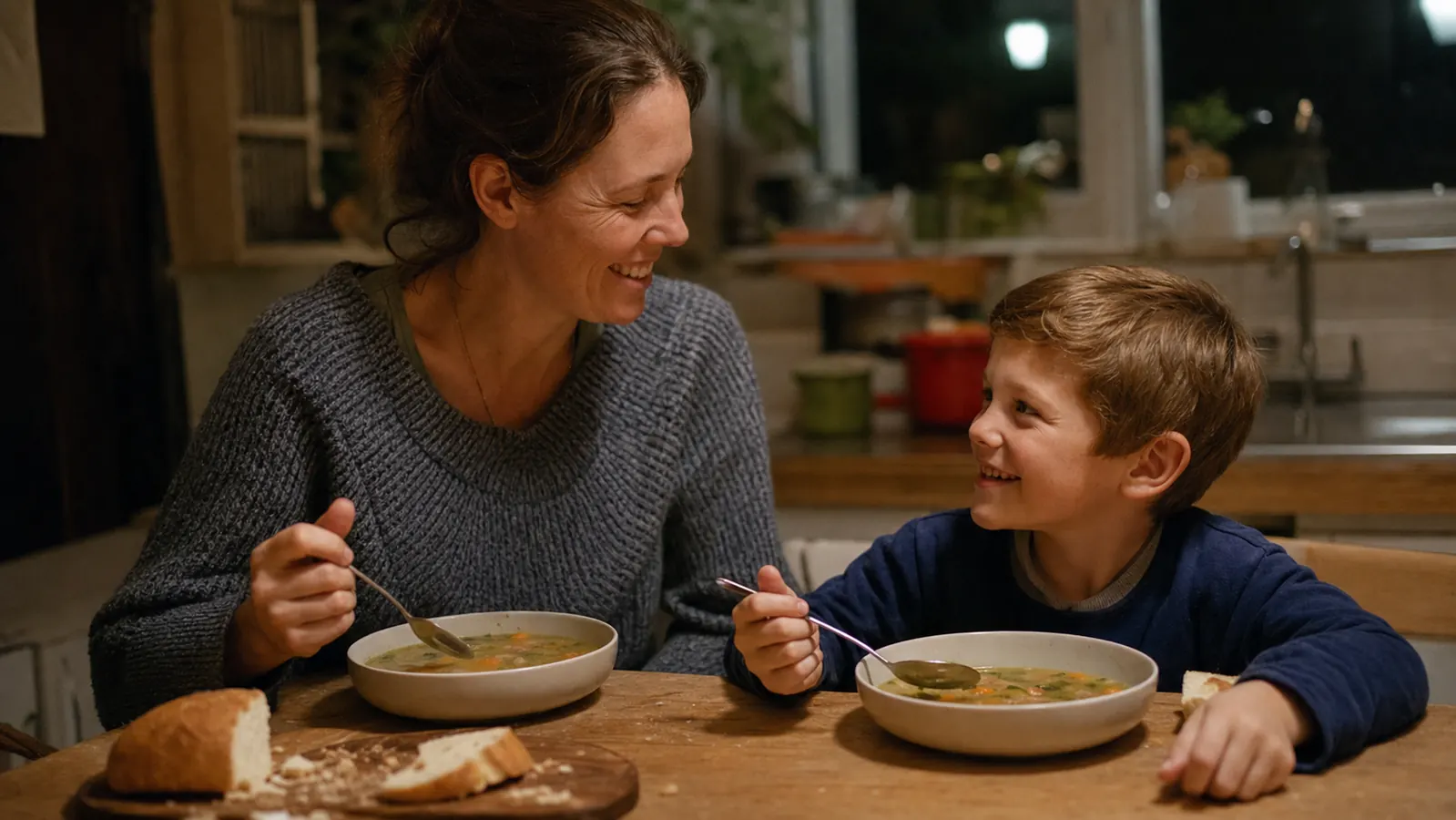 A mother and young son at a kitchen table eating soup together on a weeknight, the wrist brace no longer visible