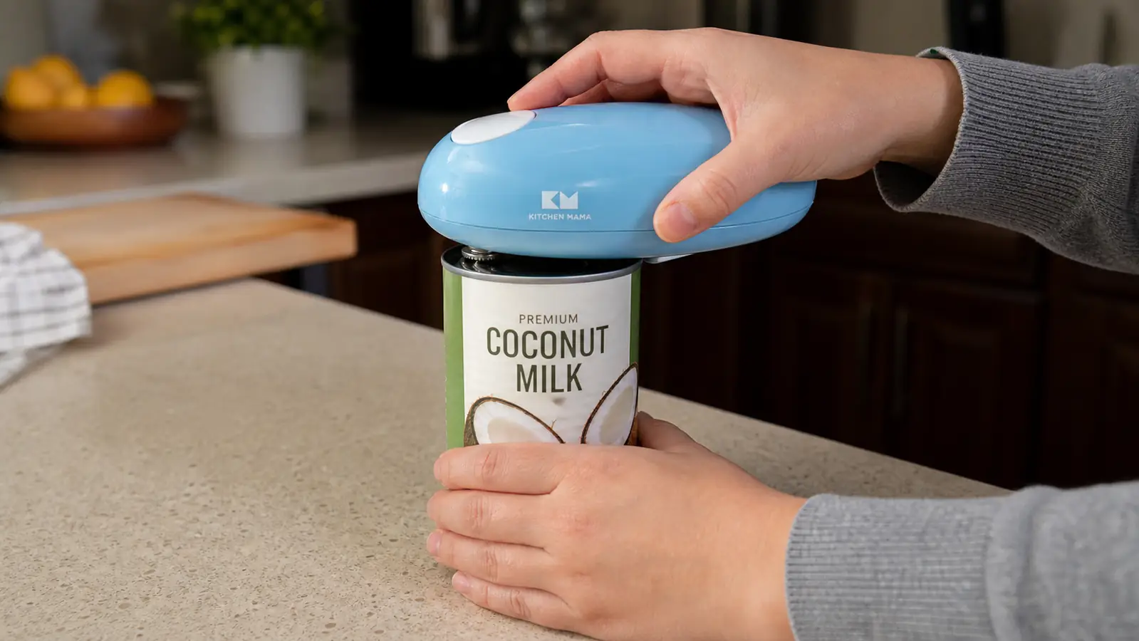 A hand steadying a tall can of coconut milk with one hand while the electric can opener runs on top of it with the other