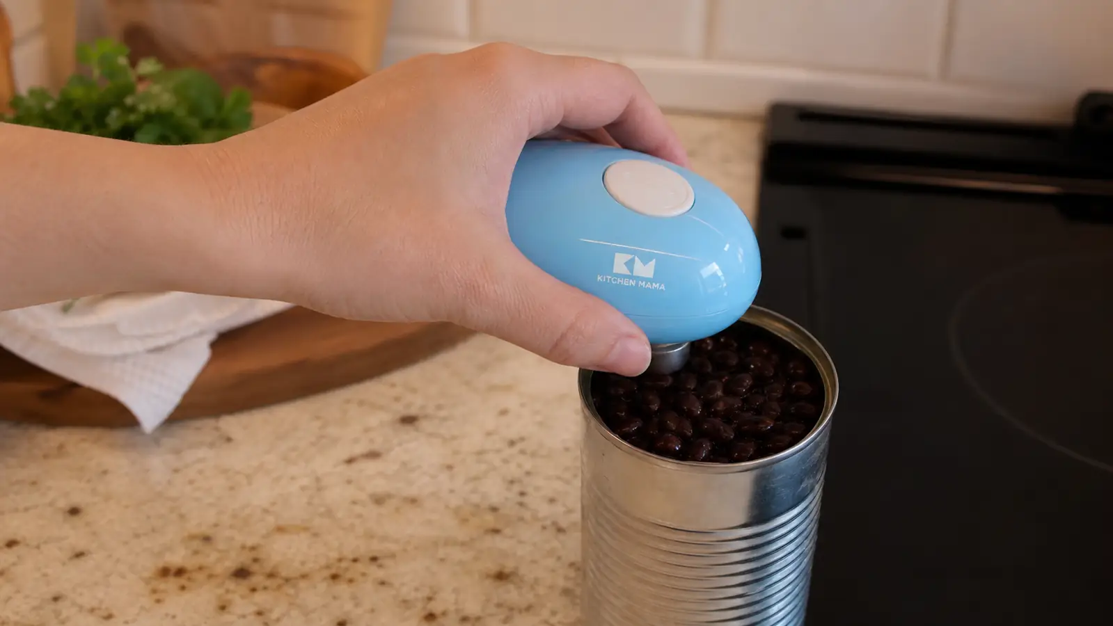 A hand pressing the automatic electric can opener down onto the rim of an open can of black beans, opener clamped to the lid