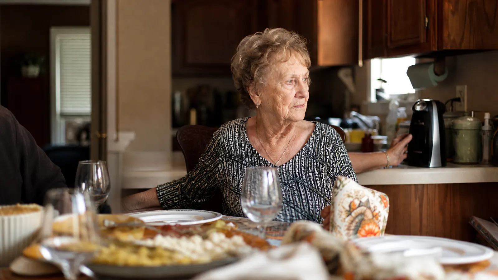 An older woman with mild hand arthritis using an electric can opener at a kitchen table set for Sunday dinner