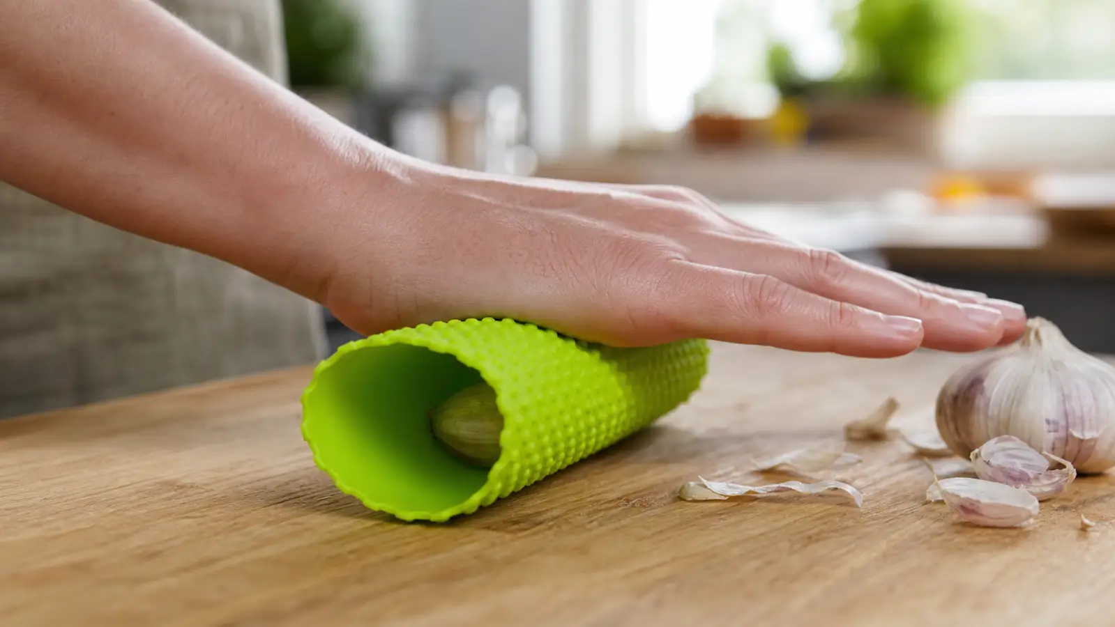Close-up of a hand rolling an unpeeled garlic clove inside the rubber peeler sleeve on a wood counter