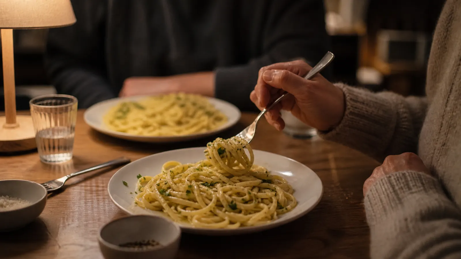 Two plates of garlic butter pasta on a small kitchen table set for a weeknight dinner