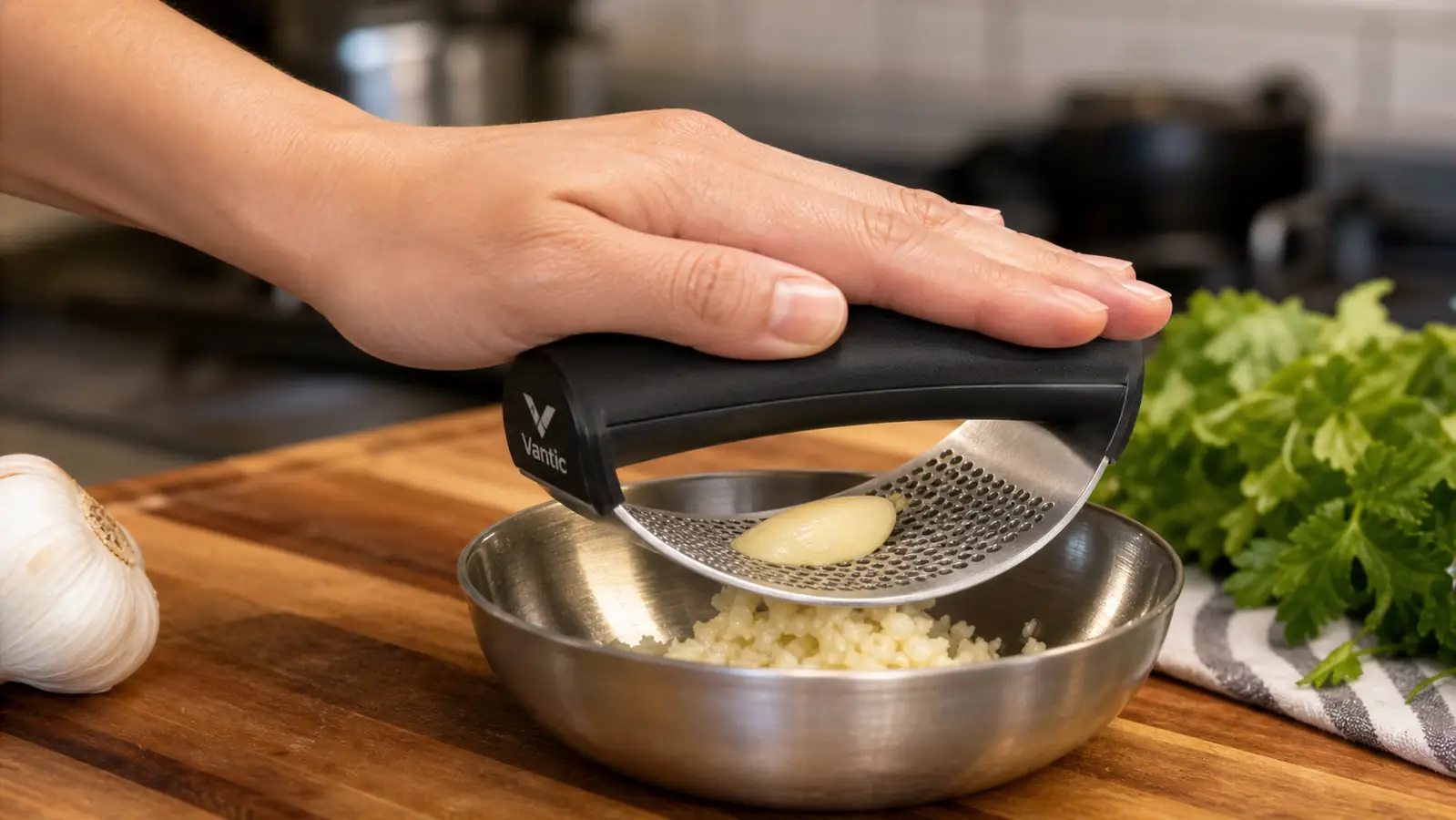 Hand rocking the stainless garlic press down onto a peeled clove over a small prep bowl on a wood counter