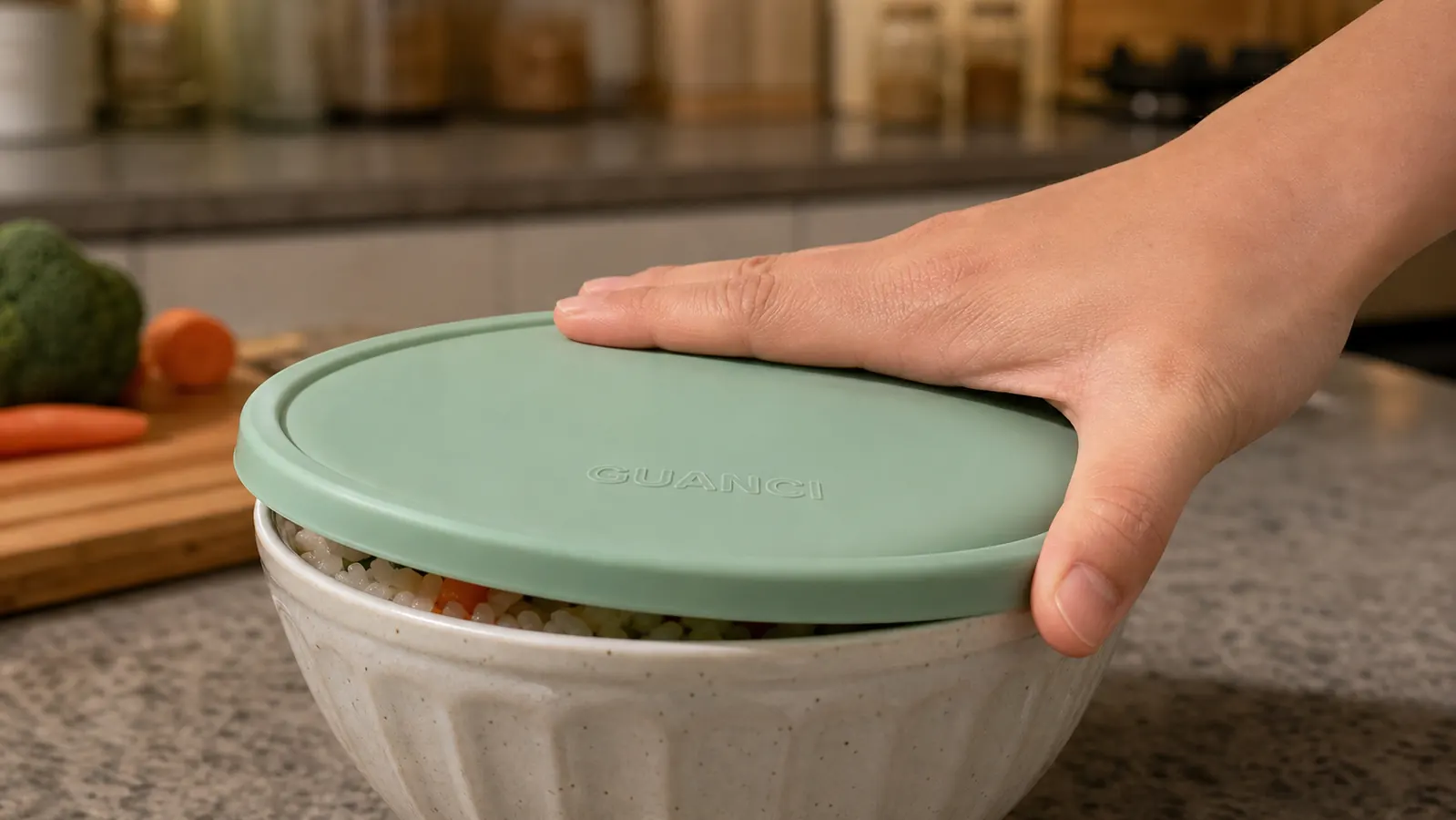 A hand pressing a silicone lid down around the rim of a bowl of leftover rice to seal it