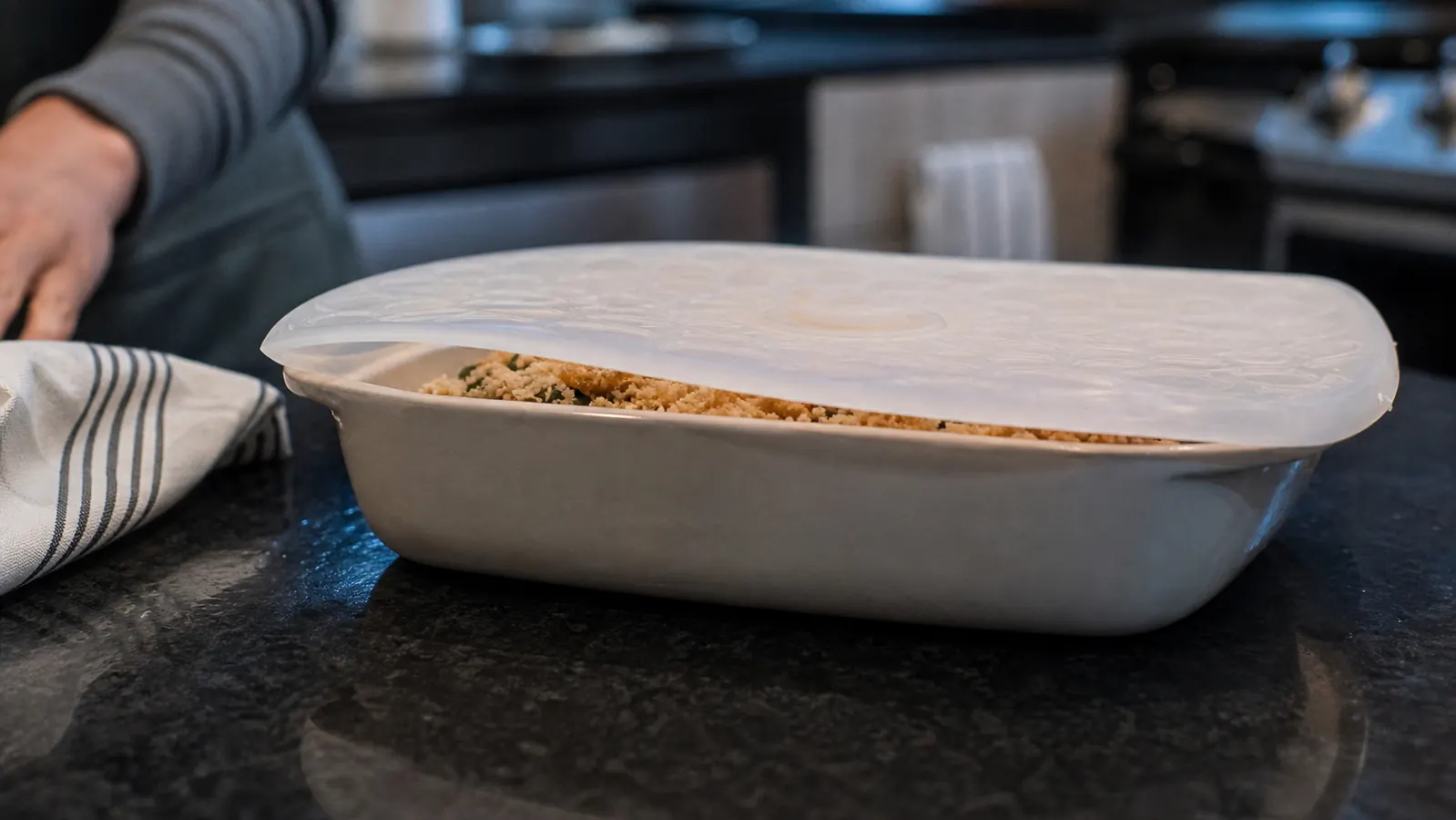 A large silicone lid slipping off the rim of a rectangular casserole dish left slightly ajar on the counter